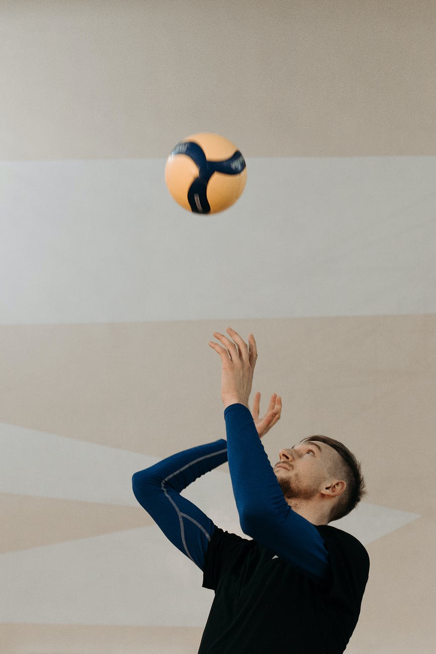 photo of a man in a black shirt tossing a volleyball
